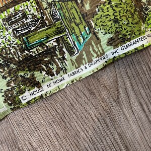 K&ouml;nnte beinhalten: Nahaufnahme eines gr&uuml;nen und braunen Stoffes mit einem sich wiederholenden Muster aus H&auml;usern und B&auml;umen. Der Stoff hat einen wei&szlig;en Rand mit dem Text "HOUSE N' HOME FABRICS & DRAPERIES INC. GUARANTEED WASHED"