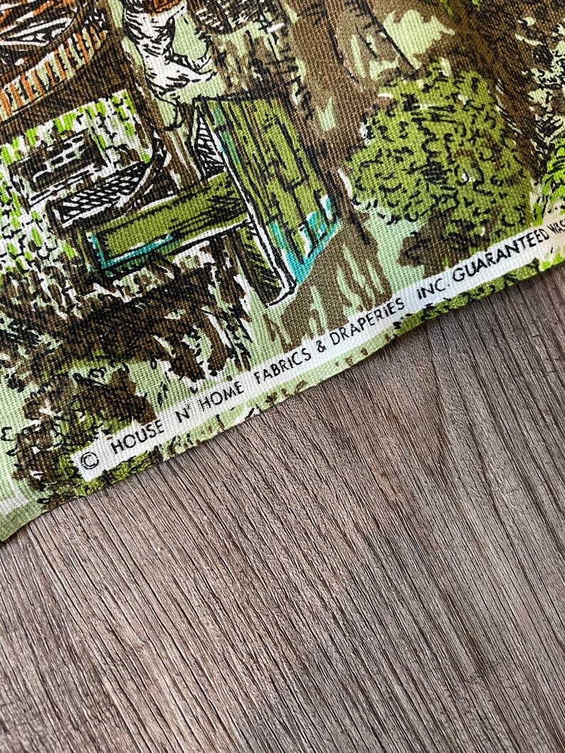 K&ouml;nnte beinhalten: Nahaufnahme eines gr&uuml;nen und braunen Stoffes mit einem sich wiederholenden Muster aus H&auml;usern und B&auml;umen. Der Stoff hat einen wei&szlig;en Rand mit dem Text "HOUSE N' HOME FABRICS & DRAPERIES INC. GUARANTEED WASHED"
