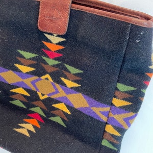 May include: Black tote bag with a brown leather handle and a colorful geometric pattern. The bag has a leather tag that says "Handbags by".