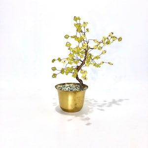 May include: A small, green beaded tree in a gold pot. The tree is made of wire and beads, and the pot is a simple, round shape.