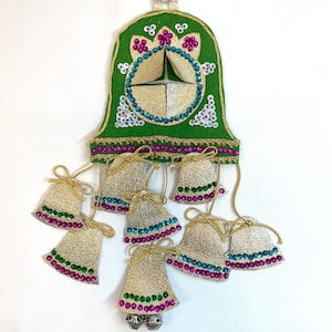 May include: A green bell-shaped ornament with gold and silver accents, adorned with small bells and decorative tassels. The ornament features a gold and silver center design, and is embellished with pink, blue, and white sequins. A festive, handcrafted item.