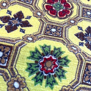 May include: Yellow fabric with a repeating pattern of brown, red, and green floral designs. The fabric has a textured surface.