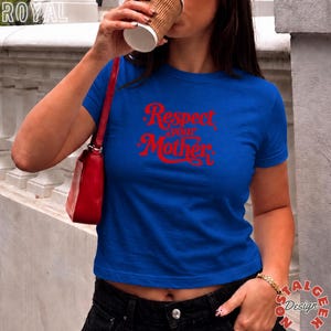 May include: A royal blue short-sleeved t-shirt featuring the red text Respect your Mother printed on the front. The shirt is paired with a bright red shoulder bag and dark denim jeans, creating a casual look with a bold graphic design element.