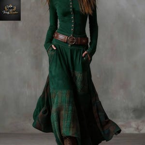 May include: A long, emerald green dress with long sleeves and a button-down bodice. The dress features a brown leather belt with a decorative buckle and plaid accents on the skirt. The dress has pockets.