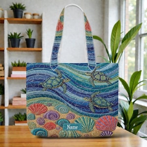 May include: A blue tote bag featuring a sea turtle design. The bag has a white handle and a colorful illustration of sea turtles swimming in the ocean, with seashells and sand at the bottom. The word "Name" is printed on a blue seashell.