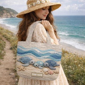May include: A quilted tote bag featuring a beach scene with blue sea turtles, waves, and sand. The bag has a light beige background with blue and white waves. The text "YOUR NAME" is on the bottom of the bag. The bag is carried by a person wearing a straw hat.