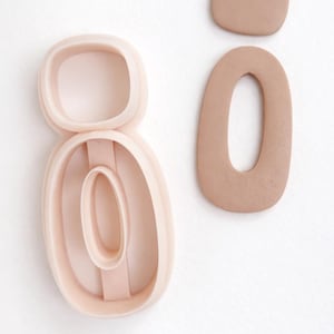 Può includere: Un set di taglierine per orecchini in argilla polimerica rosa chiaro con un orecchino in argilla abbinato e un piccolo pezzo di argilla. Il set di taglierine ha la forma di un ovale. I pezzi di argilla sono di colore marrone chiaro.
