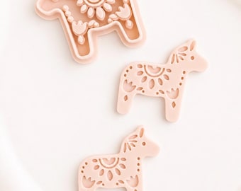 May include: Three light peach-colored horse-shaped cookie cutters of varying sizes. Each cutter features a detailed embossed floral and geometric pattern on the surface, including stylized petals, dots, and curved lines within the horse silhouette.