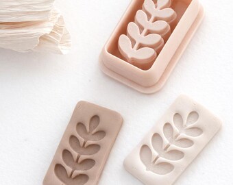May include: A collection of three leaf-shaped molds in varying shades of beige and brown. One mold is a complete leaf design, another is an imprint, and the third is a leaf-shaped mold within a rectangular frame. The molds are on a white surface.