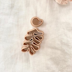 Puede incluir: Dos cortadores de galletas, uno con forma de hoja y el otro con forma de lágrima, están sobre un fondo de tela beige.