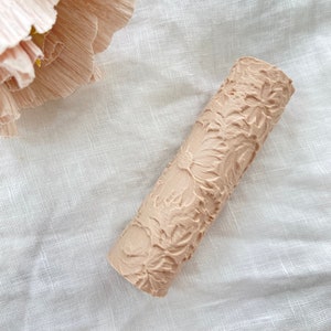 Peut inclure: Un rouleau à pâtisserie beige avec un motif floral. Le rouleau à pâtisserie est en bois et a une surface texturée.