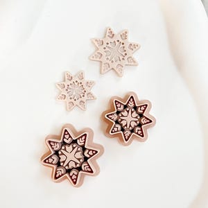 Peut inclure: Quatre objets décoratifs en forme d'étoile avec des motifs complexes. Les objets sont de tailles et de nuances de rose et de marron variables. Les formes d'étoiles ont un motif détaillé de feuilles et de cœurs. Les objets sont disposés sur une surface blanche.