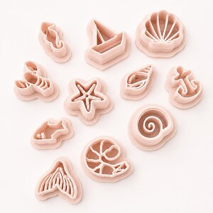 Puede incluir: Un conjunto de once cortadores de galletas de plástico rosa claro con motivos náuticos y marinos, que incluyen un caballito de mar, un velero, una vieira, una langosta, una estrella de mar, una caracola, un ancla, un pez, una concha espiral, un camarón y una cola de sirena.