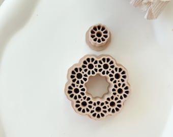 May include: Two brown, decorative, geometric, circular, lace-like cookie cutters. The larger cutter is a ring shape with a smaller circle in the center. The smaller cutter is a solid circle with a geometric design.