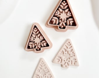 May include: Four light brown Christmas tree-shaped cookie cutters. Two cutters have a snowflake design, and two have a snowflake and star design. The cutters are made of plastic and are different sizes.