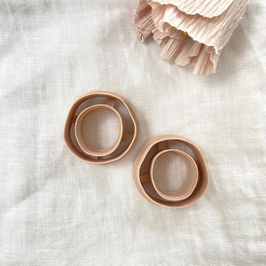 May include: Two light brown silicone donut-shaped baking molds. The molds are nested together, with the smaller mold inside the larger mold.