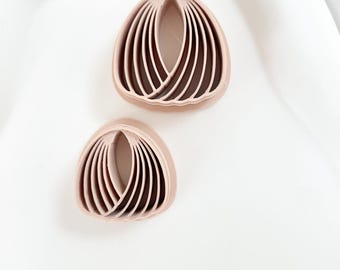May include: Two light pink, petal-shaped polymer clay cutters. The cutters have a series of curved lines that create a layered effect. The cutters are placed on a white surface.