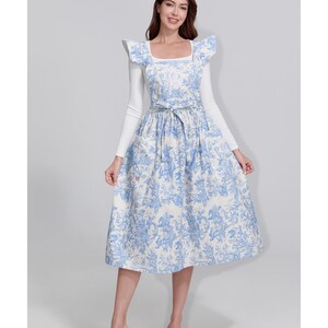 May include: A light blue and white patterned dress with a square neckline and a matching belt. The dress features a floral design and is paired with a white long-sleeved top. The dress is knee-length.