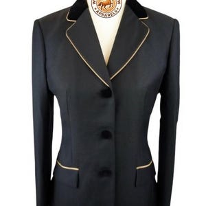 May include: A black equestrian show jacket with a velvet collar and gold trim. The jacket has three buttons and two front pockets. The logo "WESTERN GLOW APPARELS" is visible on the collar.