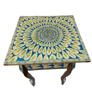 May include: A square side table featuring a vibrant blue and yellow inlaid pattern on the tabletop and sides. The design consists of repeating teardrop shapes radiating from the centre. The table is supported by four curved wooden legs.