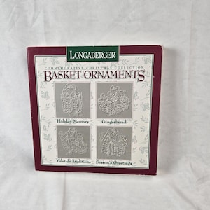 Puede incluir: Una caja cuadrada para adornos de cesta de la Colección Conmemorativa de Navidad de Longaberger. La caja presenta un borde rojo oscuro, un centro blanco con un patrón de hojas de acebo y cuatro ilustraciones de adornos de cesta etiquetadas como Holiday Memory, Gingerbread, Yuletide Traditions y Season's Greetings.