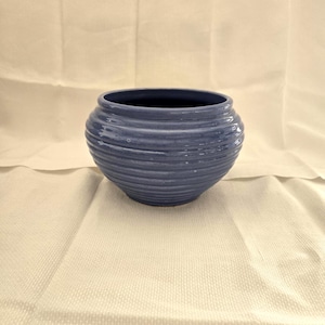 Könnte beinhalten: Eine blaue Keramikschale mit gerippter Außenseite. Die Schale hat eine abgerundete Form und einen dunkelblauen Innenraum. Die Schale steht auf einer weißen Oberfläche.