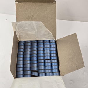 May include: A cardboard box filled with numerous spools of blue thread. The spools are neatly arranged and wrapped in a thin, light blue thread. The box is open, revealing the contents, and lined with white tissue paper.