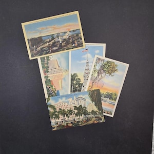 May include: A collection of vintage postcards featuring scenes from Florida. The postcards depict various landmarks, including buildings, waterfront views, and landscapes. The postcards are arranged on a black surface.