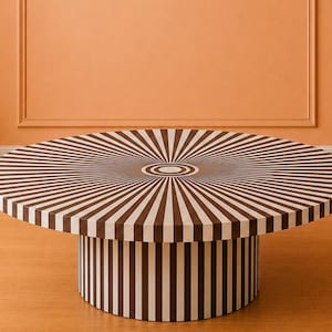 May include: A round coffee table featuring a dark brown and white sunburst pattern on the top surface. The cylindrical base is decorated with vertical dark brown and white stripes that wrap around the entire circumference of the table support.