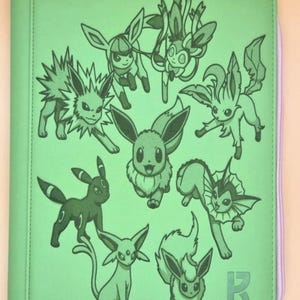 Peut inclure: Un classeur zippé vert clair avec une impression graphique vert foncé représentant divers personnages de l'évolution d'Évoli. La couverture avant affiche plusieurs créatures dans différentes poses, avec une petite lettre R en bas à droite.