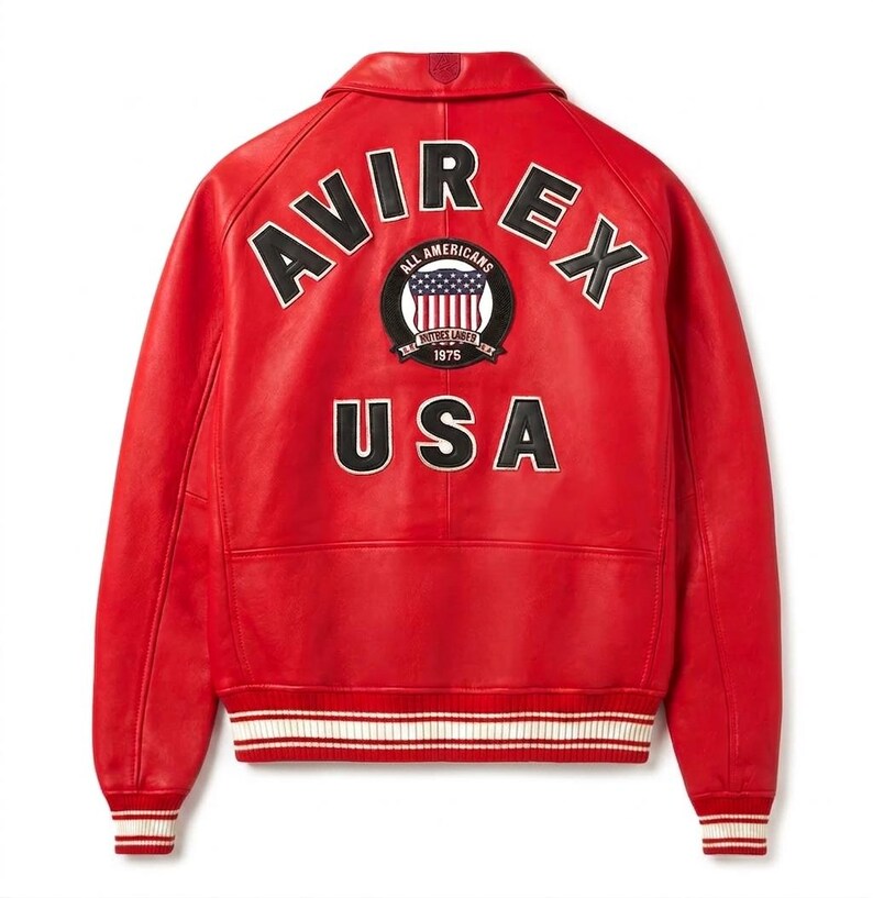 Puede incluir: Chaqueta de cuero roja con letras y parches blancos y negros. La parte trasera de la chaqueta presenta la palabra "AVIREX" arqueada en la parte superior, un parche circular con las palabras "ALL AMERICANS" y "USA" en la parte inferior.