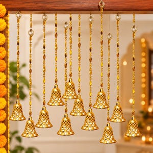 Puede incluir: Un adorno colgante con doce campanas de metal dorado suspendidas de una barra de madera horizontal. Cada campana está sujeta a una larga cadena de cuentas doradas y presenta un delicado e intrincado patrón de celosía recortada.
