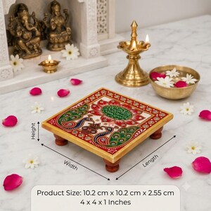May include: A square wooden platform with four short legs, featuring a hand-painted design of a central lotus flower and two peacocks in red, green, and gold tones with embedded crystals. The product measures 10.2 cm x 10.2 cm x 2.55 cm.