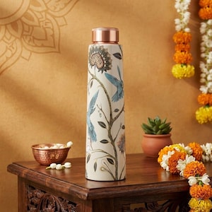 May include: A cylindrical water bottle with a cream-colored base featuring a detailed botanical print of blue birds, brown flowers, and dark green leaves. The bottle has a metallic copper-toned screw-top lid and a smooth, straight-sided body.