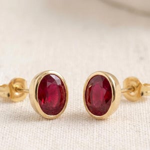 Peut inclure: Une paire de boucles d'oreilles à clous avec des rubis rouge foncé taille ovale sertis dans des chatons en or jaune poli. Chaque boucle d'oreilles comprend une tige en or jaune assortie et un fermoir papillon pour la fixation au lobe.