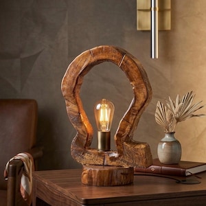 Könnte beinhalten: Eine einzigartige Tischlampe aus Holz, die ein warmes Licht ausstrahlt. Die Lampe hat einen geschnitzten Holzrahmen und eine Glühbirne im Vintage-Stil. Sie steht auf einem dunklen Holztisch und schafft eine gemütliche und stilvolle Atmosphäre. Ca. 30 cm hoch.