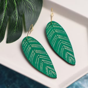 May include: A pair of green leaf-shaped earrings with gold wire hangers. The leaves have a white and green striped pattern.