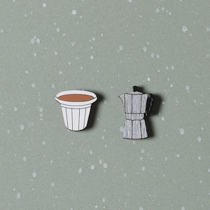 May include: A white ceramic coffee cup with brown coffee inside and a gray wooden coffee pot.