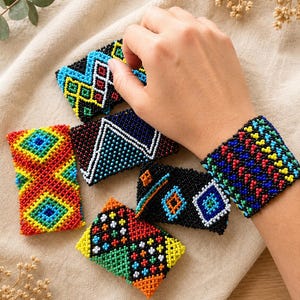 May include: A collection of rectangular beaded bracelets featuring intricate geometric patterns in vibrant colours including red, blue, yellow, green, and black. One bracelet is worn on the wrist, while four others are displayed nearby.