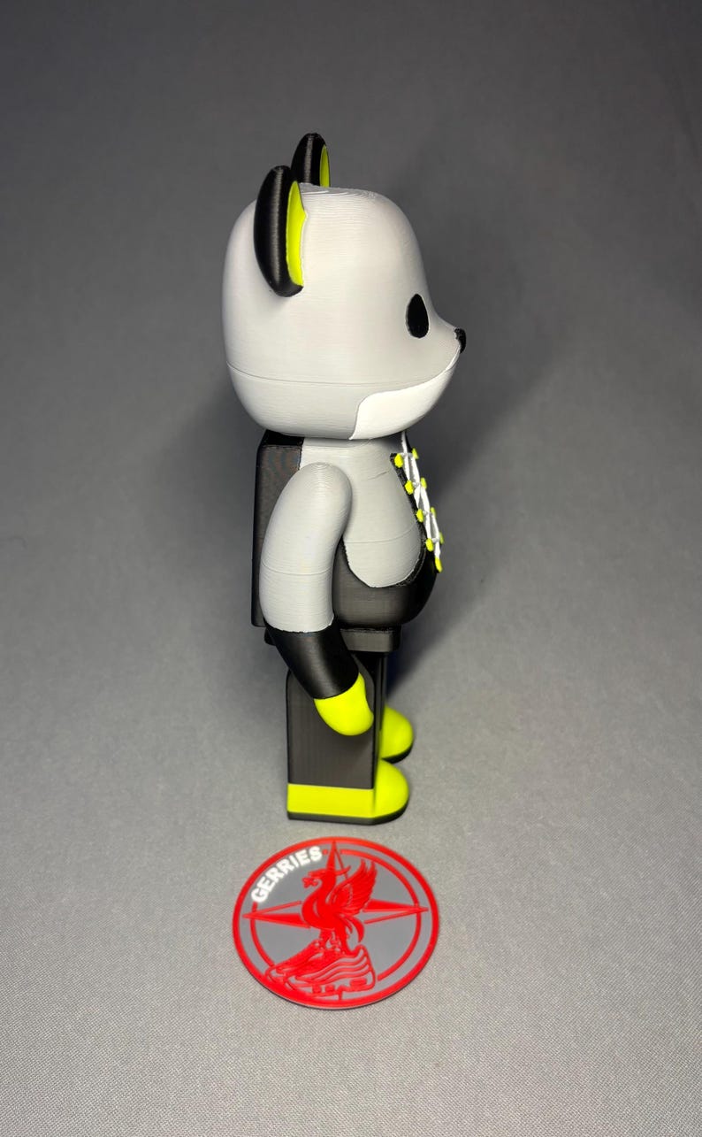 May include: A gray and black bear-shaped figurine with yellow accents on the ears and feet. The figurine has a white chest and a black torso. A red and gray logo with the word "GERRIES" is at the base.