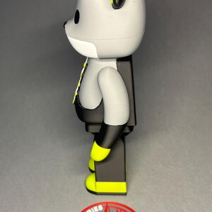 May include: A gray and black bear-shaped figurine with yellow accents on the ears and feet. The figurine has a white face and a black vest. A red and gray logo with the word "GERRIES" is at the base.