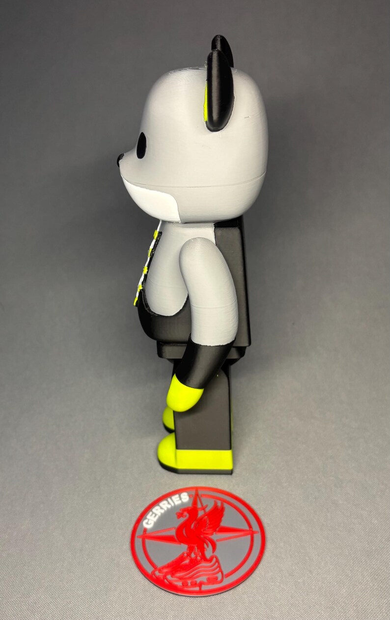 May include: A gray and black bear-shaped figurine with yellow accents on the ears and feet. The figurine has a white face and a black vest. A red and gray logo with the word "GERRIES" is at the base.