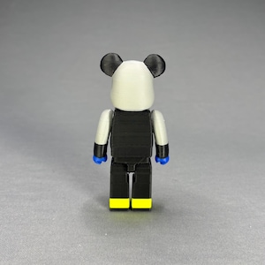 Puede incluir: Figura impresa en 3D con tem&aacute;tica de panda. La figura tiene una cabeza blanca con orejas negras, un torso negro y piernas negras con pies amarillos. Los brazos son plateados y las manos azules. Dise&ntilde;o estilizado y en bloques.