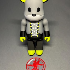 May include: A gray and black mouse-themed figurine with yellow accents on the ears, hands, and feet. The figurine has a white face and a laced-up design on the chest. A red and gray logo with the word "GERRIES" is at the base.