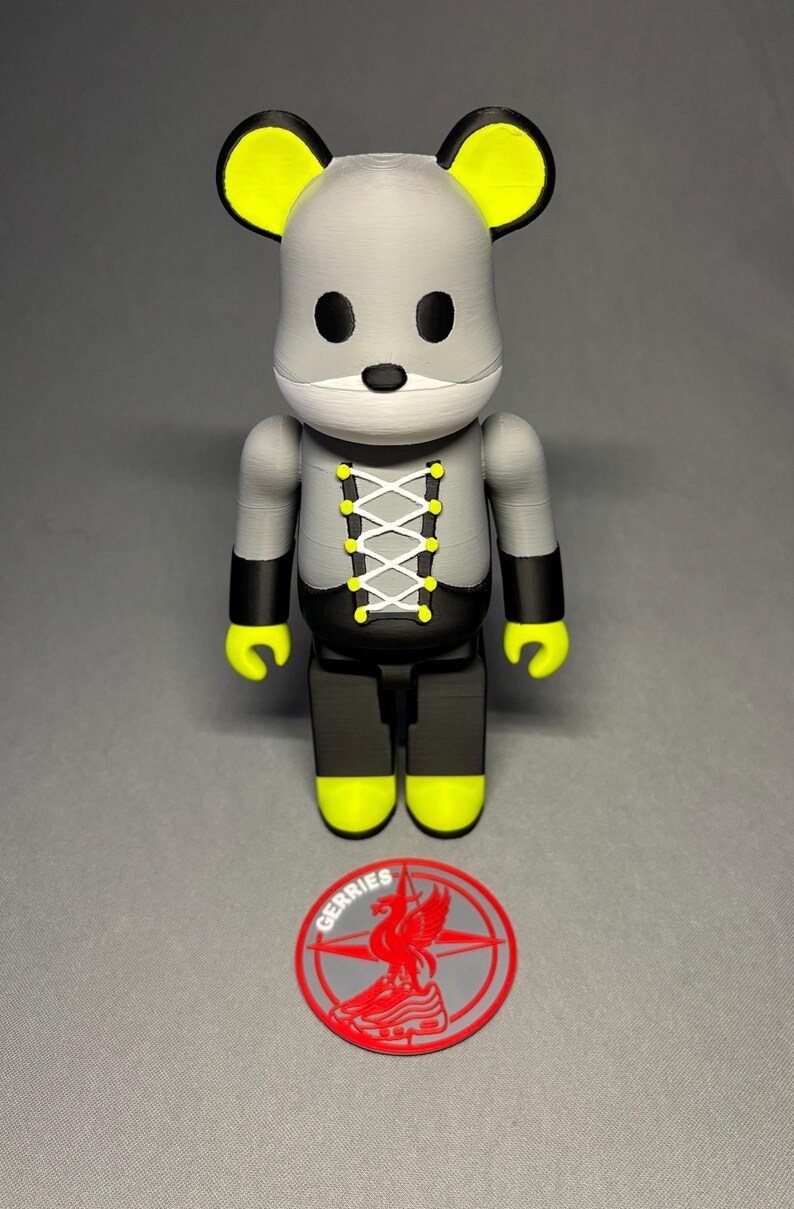 May include: A gray and black mouse-themed figurine with yellow accents on the ears, hands, and feet. The figurine has a white face and a laced-up design on the chest. A red and gray logo with the word "GERRIES" is at the base.