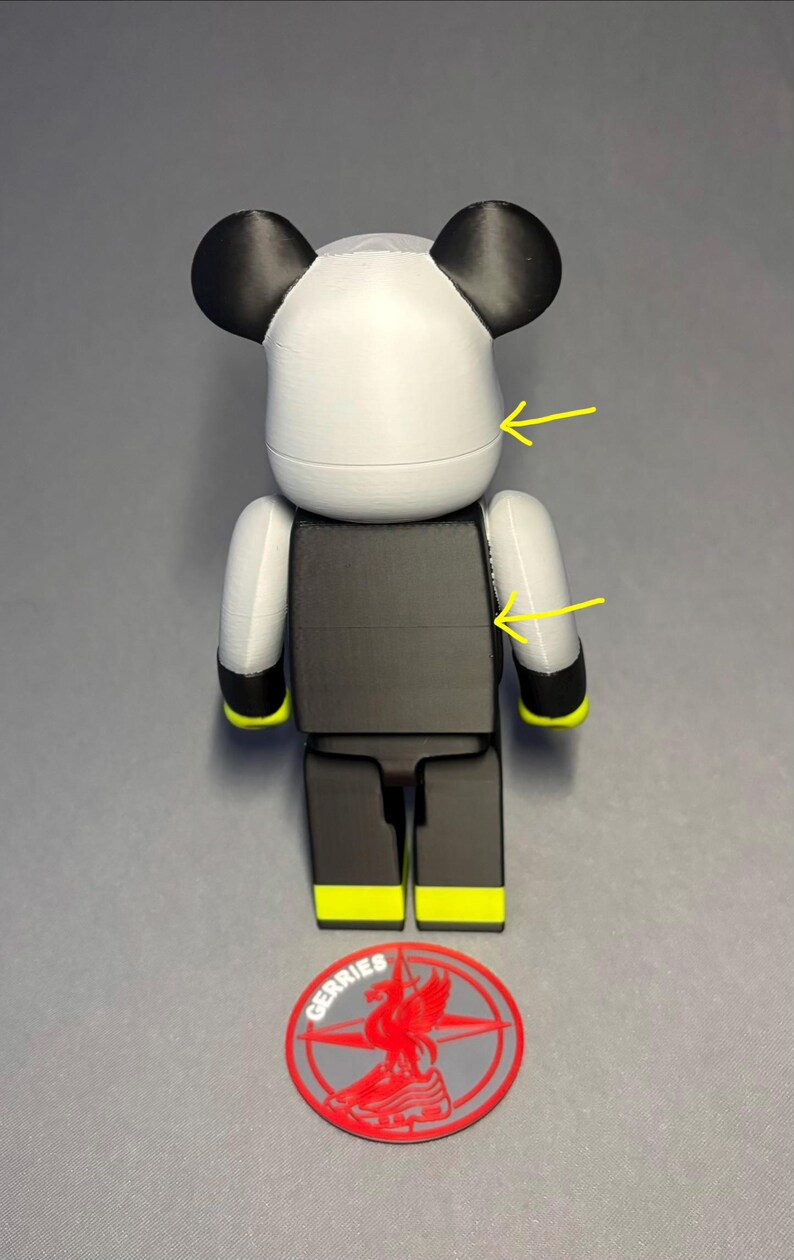 May include: A stylized bear-shaped figurine in white, black, and yellow. The figure has a white head with black ears, a black torso, and black legs with yellow accents. A red and gray logo is at the base.