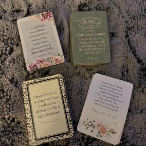 Puede incluir: Cuatro tarjetas rectangulares con escrituras religiosas e ilustraciones florales. Una tarjeta muestra 1 Corintios 13:4, 7, otra 2 Corintios 8:9, una tercera el Salmo 16:8 y la cuarta el Salmo 139:23-24. Las tarjetas tienen bordes blancos, verdes y negros.
