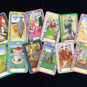May include: A collection of eleven rectangular tarot cards featuring colorful, detailed illustrations of various figures, landscapes, and architectural scenes. Each card is framed with a decorative border and includes text labels at the bottom.