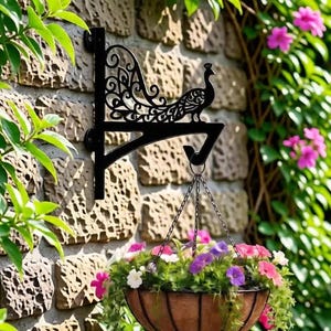 Könnte beinhalten: Schwarzer Metall-Pfausträger für einen Hängekorb, montiert an einer Steinmauer. Die Halterung trägt einen Hängekorb voller bunter Blumen. Grünes Laub und rosa Blüten umrahmen die Szene und schaffen eine lebendige Gartenästhetik.