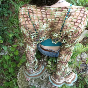 May include: A long-sleeved crochet shrug featuring an open-knit grid pattern in shades of brown, olive green, and light mint green. The garment has flared, bell-shaped cuffs with a solid brown and mint green border at the bottom edges.
